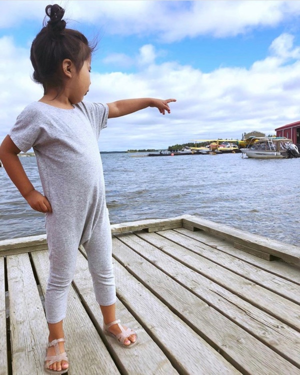 Little girl in grey romper pointing toward the water.