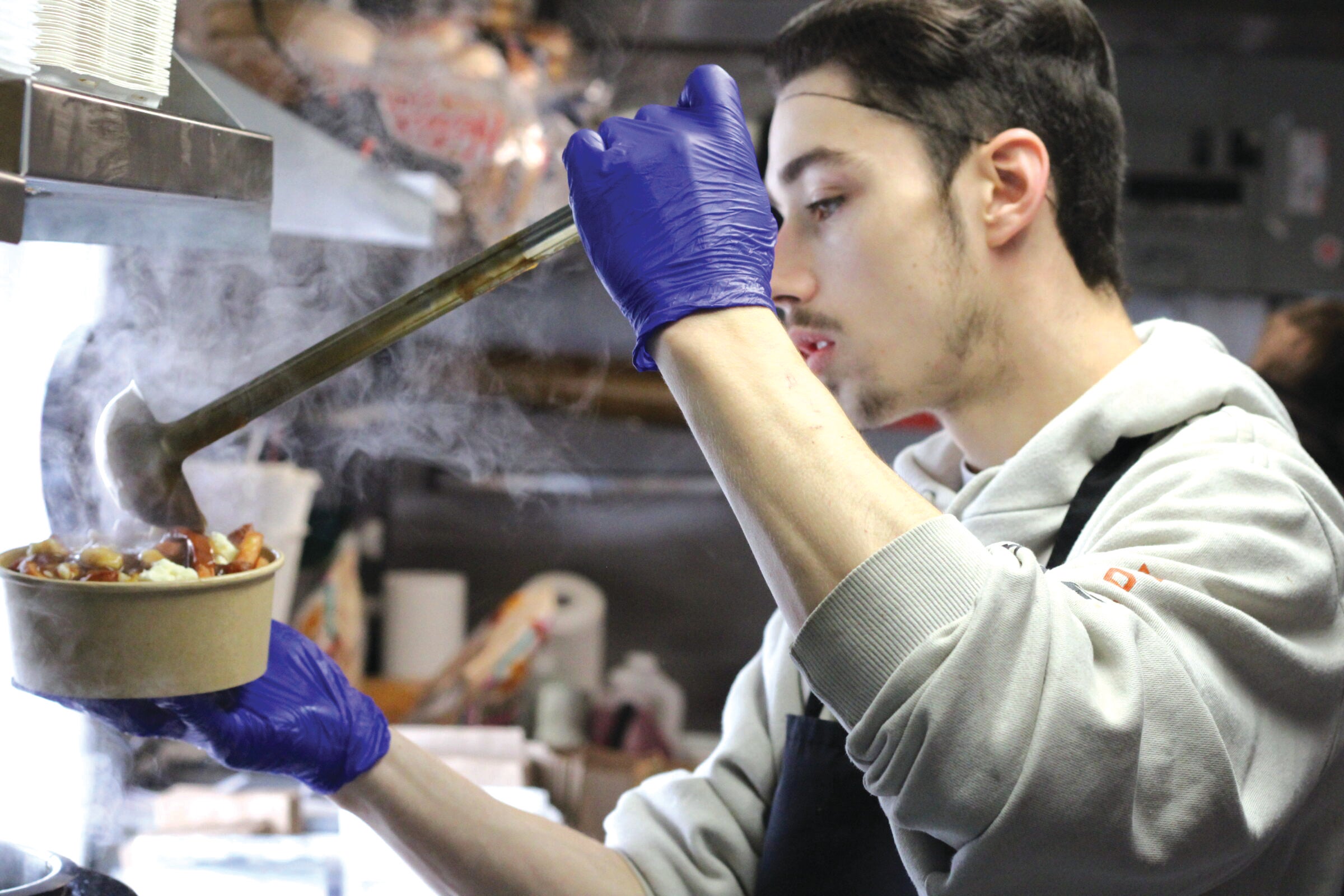 Person pouring gravy on Poutine