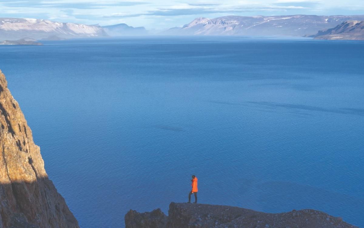 A tourist stands on a cliff, overlooking the water. 