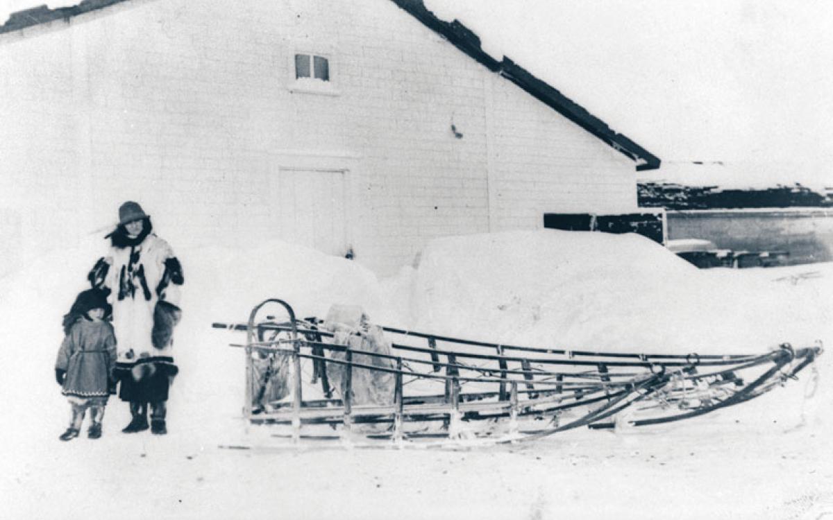 A woman and child stand in front of the Bone House on Herschel Island, where two Inuit men were hanged for murder in 1924. PWNHC: N-1991-041-0065