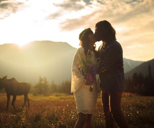 This kissing couple travelled all the way up from the sunny beaches of Hawaii to the wild backcountry of the North for their one-of-a-kind destination wedding. The moose who's wandering through their wedding photo apparently had no objections to the union.