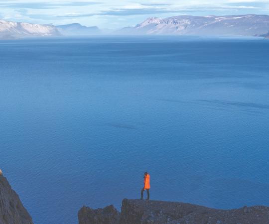 A tourist stands on a cliff, overlooking the water. 